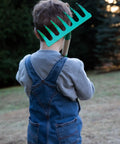 Child holding Kids Garden Tool Set 4 Piece Rake Spade Hoe And Leaf Rake With Real Wood Handles And Steel Heads, outdoor setting.