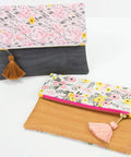 Two floral fabric clutches with tassels, one black and pink, the other yellow and pink, on a white background.