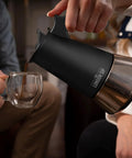 Stainless Steel Stovetop Espresso Maker Moka Pot With Matte Black Finish 10 Cup being used to pour coffee into a glass cup.
