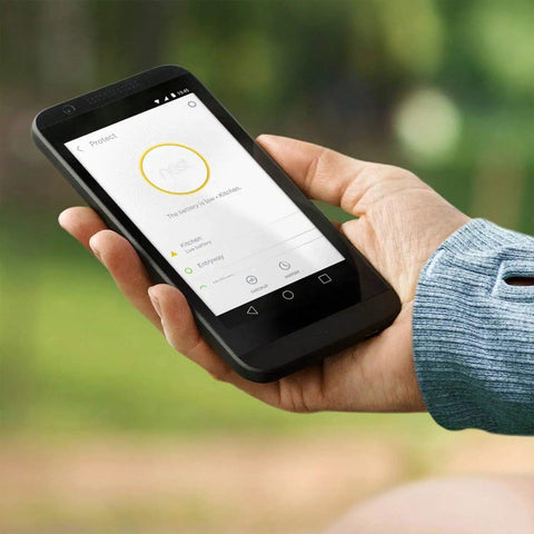 Person holding smartphone showing Smart Smoke Alarm With Built In Carbon Monoxide Detector Wired 120V Voice Alerts And Phone Notifications