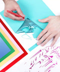 Hands using a weeding tool on Electric Red Siser EasyWeed Heat Transfer Vinyl Roll 5 Feet on colored papers.