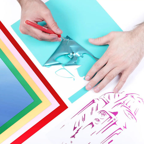 Hands using a weeding tool on Electric Red Siser EasyWeed Heat Transfer Vinyl Roll 5 Feet on colored papers.