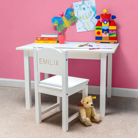 Children's white desk and chair with colorful art supplies and toys against a pink wall, featuring 'Emilia' personalization on the chair.