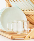 Heavy Duty Bamboo Dish Drying Rack Three Tier Collapsible Wooden Drainer With Utensil Holder holding glass mugs and plates.