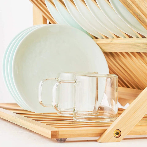 Heavy Duty Bamboo Dish Drying Rack Three Tier Collapsible Wooden Drainer With Utensil Holder holding glass mugs and plates.