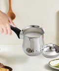 Person holding stainless steel 720ml Turkish Coffee Pot and Butter Warmer Pan on kitchen counter with lid nearby.