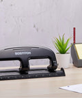 Bostitch 20-sheet 3-hole punch, metal construction, black; desk scene with plant and note organizer.
