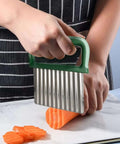 Front view of green-handled stainless steel wave crinkle cutter slicing orange carrot on parchment paper