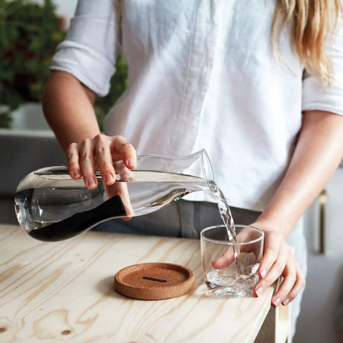 Person pouring water from a carafe with Charcoal Water Filter Sticks For Dope Tasting Hydration Inspired By Old Japanese Tradition Lasts Six Months Per Stick Perfect For Your Reusable Water Bottle And Everyday Sips into a glass.