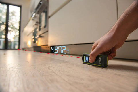 Pro 20 Meter Laser Distance Meter With Clear Digital Screen And Continuous Measurement Mode measuring 4.97m on wooden floor.