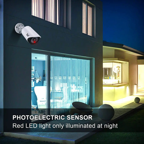 Realistic Fake Surveillance Camera 2 Pack With LED Light installed on outdoor wall of modern house, red LED visible at night.