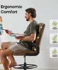 Man using tall drafting chair with padded flip up armrests, ergonomic leather backrest, and adjustable footrest ring for standing desks
