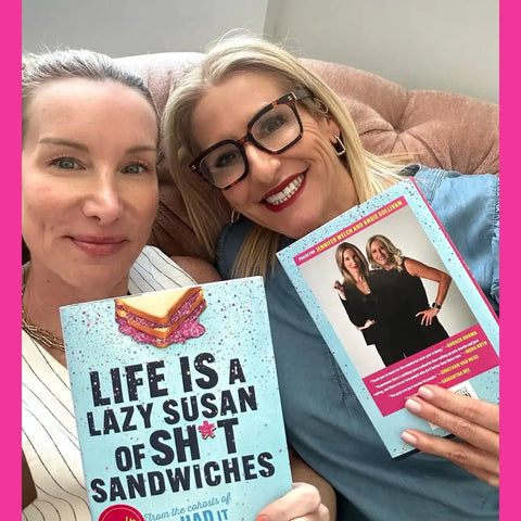 Two women holding the book 'LIFE IS A LAZY SUSAN OF STRAIGHT FIRE ADVICE AND KEEPING IT REAL WISDOM' in a cozy setting.