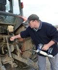 Person using Lincoln 1884 PowerLuber 20V Battery Powered Grease Gun with 36-inch hose on tractor machinery in field