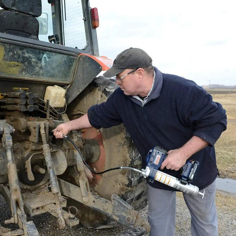 Person using Lincoln 1884 PowerLuber 20V Battery Powered Grease Gun with 36-inch hose on tractor machinery in field