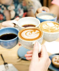 People toasting with coffee mugs, showcasing latte art and black coffee, related to Unbleached Round Disposable Coffee Filters, 600 Count, 64 Mm 2.5 Inch Size, Fits Most Drip Pots And Espresso Machines, Easy Cleanup, Absorbs Oils For Cleaner Smoother Tasting Coffee Keeps Your Cup Clean.
