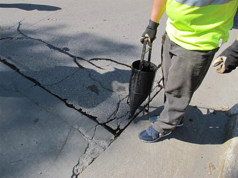 Person using 2.6 Gallon Pour Pot With Wheels For Asphalt Crack Sealant 14 Gauge Welded Steel Construction Cold Crack Sealant Applicator