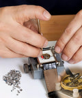 Hands using watch repair kit with 100Pcs watch battery clamp screws set for micro screw replacement in watches on a workbench.