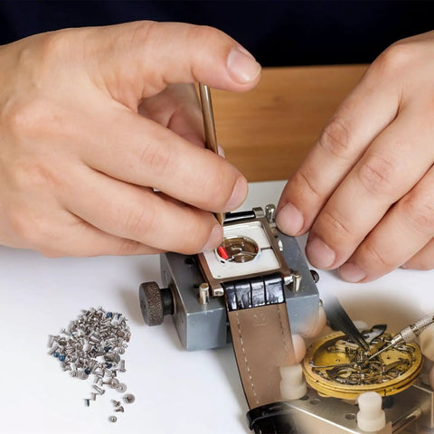 Hands using watch repair kit with 100Pcs watch battery clamp screws set for micro screw replacement in watches on a workbench.