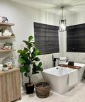 Modern bathroom with rectangular pendant light, black and gold geometric metal cage, and freestanding bathtub with plants and shelves.
