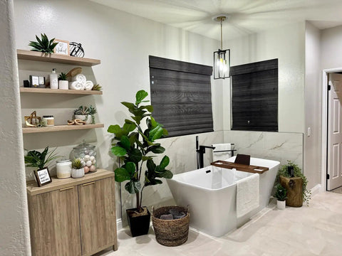 Modern bathroom with rectangular pendant light, black and gold geometric metal cage, and freestanding bathtub with plants and shelves.