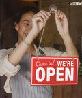 Person hanging Open And Closed Sign For Biz 10 By 6 Inches Double Sided Plastic Sign With Twine And Suction Cup Hook For Door Or Window Easy To Read Business Hours Black And Red on glass door