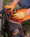 Person wearing orange knit dipped cut resistant work gloves with nitrile coated palms, handling tools from a black bag outdoors.