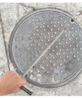 Hand using Heavy Duty Stainless Steel T Hook Drain Grabber For Manhole Covers And Heavy Grates on a manhole cover.