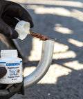 WEICON Copper Paste bottle (4.2 oz/120 g) being applied to a curved metal joint by gloved hands.