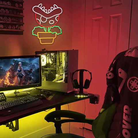 Piranha Plant LED Neon Sign Night Light For Super Mario Fans on wall in gaming room, glowing beside computer setup.