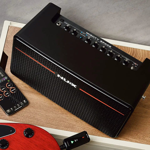 30W Wireless Modeling Guitar Amplifier With Built In IRs Dual 4 Inch Coaxial Speakers on a wooden table with remote and guitar.