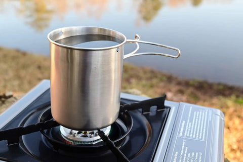Stainless Steel Canteen Water Bottle With Nested Camping Cup And Lid on a gas burner near a lake, 40oz metal canteen for outdoor use.