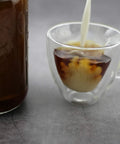 Glass cup of iced coffee with milk pouring next to jar, using Ultra Fine Stainless Cold Brew Coffee Filter For Wide Mouth Mason Jars.