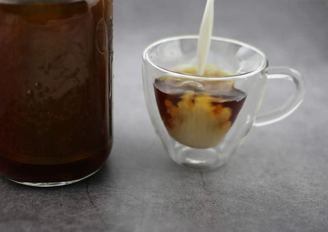 Glass cup of iced coffee with milk pouring next to jar, using Ultra Fine Stainless Cold Brew Coffee Filter For Wide Mouth Mason Jars.