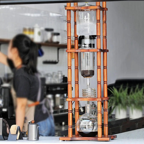 Smooth Chill Vibes All Day Retro Wood And Glass Ice Drip Coffee Maker With 105 Oz Capacity in a café setting.