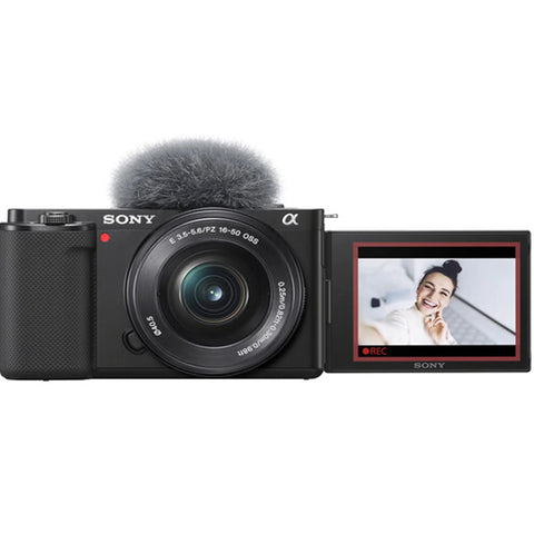 Front view of ZV-E10 Mirrorless Camera Kit With 16-50mm Lens, screen flipped, capturing a smiling person, ideal for vlogging.
