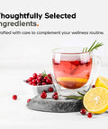Glass cup of herbal tea with lemon slices, cranberries, and rosemary on stone slab, showcasing natural ingredients.