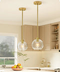 Two Pack Slick Vintage Pendant Lights With Clear Glass Globes And Gleaming Gold Canopies Adjustable Drop Length Perfect For Kitchen Islands Dining Rooms Emitting A Cozy Vibe Hardwired Installation over a kitchen island.