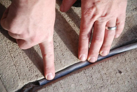 Hands installing Pre Caulking Filler Rope Backer Rod Roll Gray, 100 Foot Long, Quarter Inch Width into a concrete joint