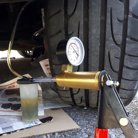 Pro Grade Two In One Brake Bleeder Kit With Handheld Vacuum Pump And Precision Pressure Gauge set up with fluid reservoir on driveway.
