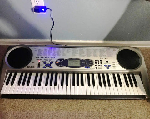 Casio LK-44 keyboard with a blue LED lit power adapter