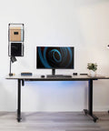 Durable Heavy Duty Freestanding Monitor Mount Desk Stand Rock Solid Height Adjustable Arm For 17 To 32 Inch Screens on a desk with lamp and plant.