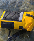 Yellow waterproof roll-top backpack with padded straps in water, showing heavy-duty design for hiking and camping.