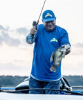 Man holding a crappie fish with Wally Marshall Signature Series Spincast Fishing Reel, showcasing fishing success on a boat.