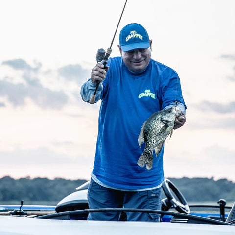 Man holding a crappie fish with Wally Marshall Signature Series Spincast Fishing Reel, showcasing fishing success on a boat.