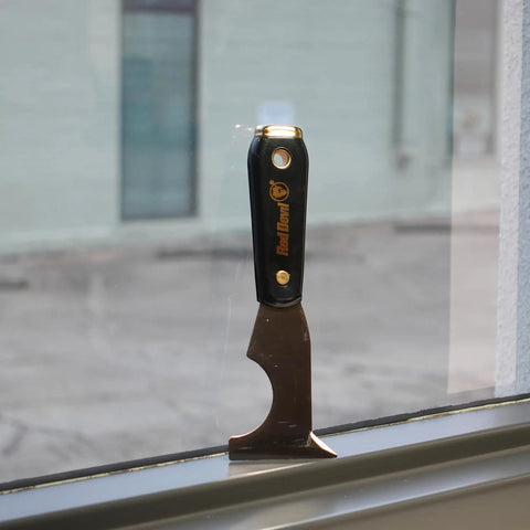 Six In One Painter Tool for DIYers with scraper, black nylon handle, and high carbon steel blade on window ledge.