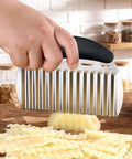 Large stainless steel crinkle cutter with black handle slicing potatoes into crinkle fries.