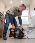 Man using 20 Volts Cordless Electric Drain Auger Equipped With Twenty Five Foot Pipe Snake to unclog toilet.