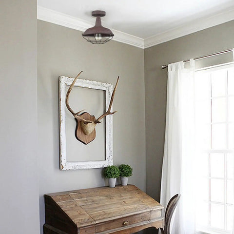 Straight Up Rustic Charm All Metal Barn Style Semi Flush Mount Ceiling Light Featuring Vintage Wire Cage Rust Finish ETL Certified above a wooden desk.