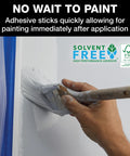 ProGrade Painter Tape With PaintBlock Technology Blue 1.5 Inch Wide Multi Surface Masking Tape Medium Adhesion 6 Rolls 1.41 In X 60 Yds for Walls and Trim shown being used on a wall with white paint and brush.